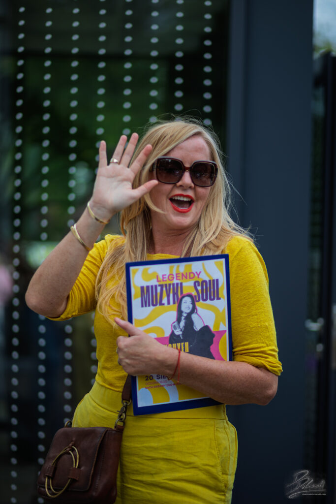 Na zdjęciu uśmiechnięta Anna Wiśniewska, Dyrektor CDT w Lubinie. Jedną ręką macha do obiektywu, a w drugiej ręce z radością prezentuje plakat z napisem „Legendy Muzyki Soul”.