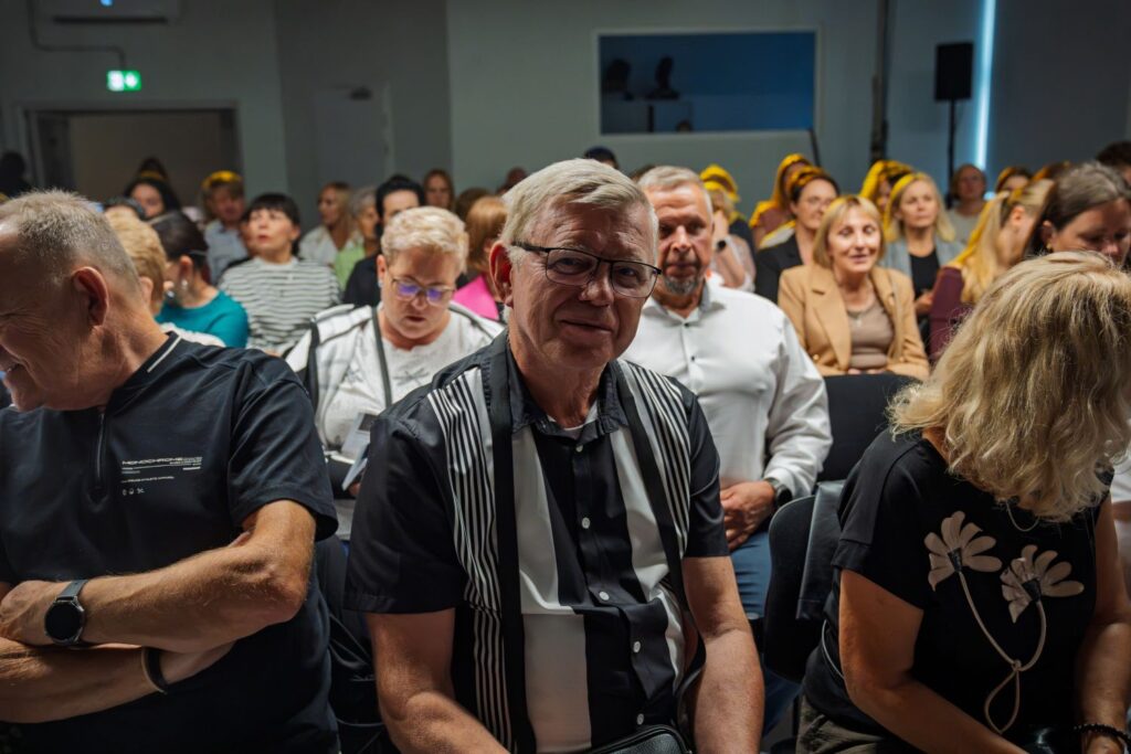 Portret starszego widza w okularach na tle publiczności zgromadzonej w sali.