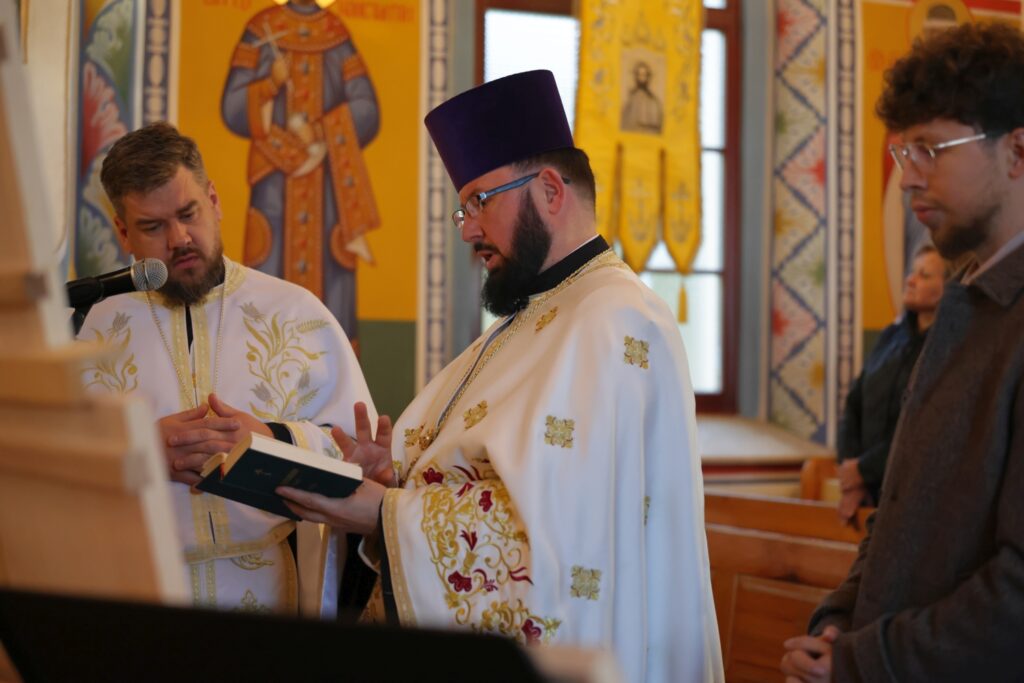 Duchowni w uroczystych szatach czytający z ksiąg w cerkwi.