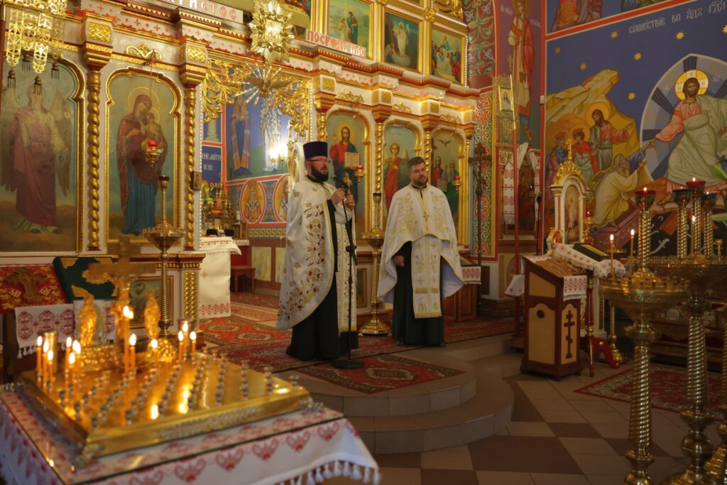 Widok na ołtarz i duchownych w bogato zdobionej cerkwi.