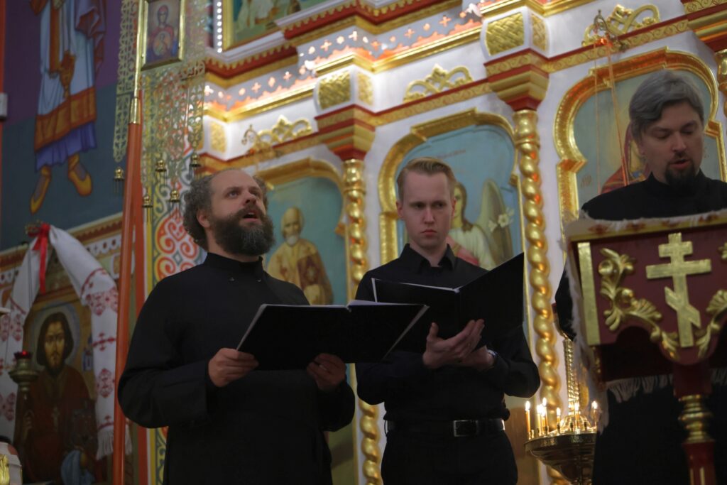 Śpiewacy w czarnych szatach patrzą w nuty podczas występu w cerkwi.