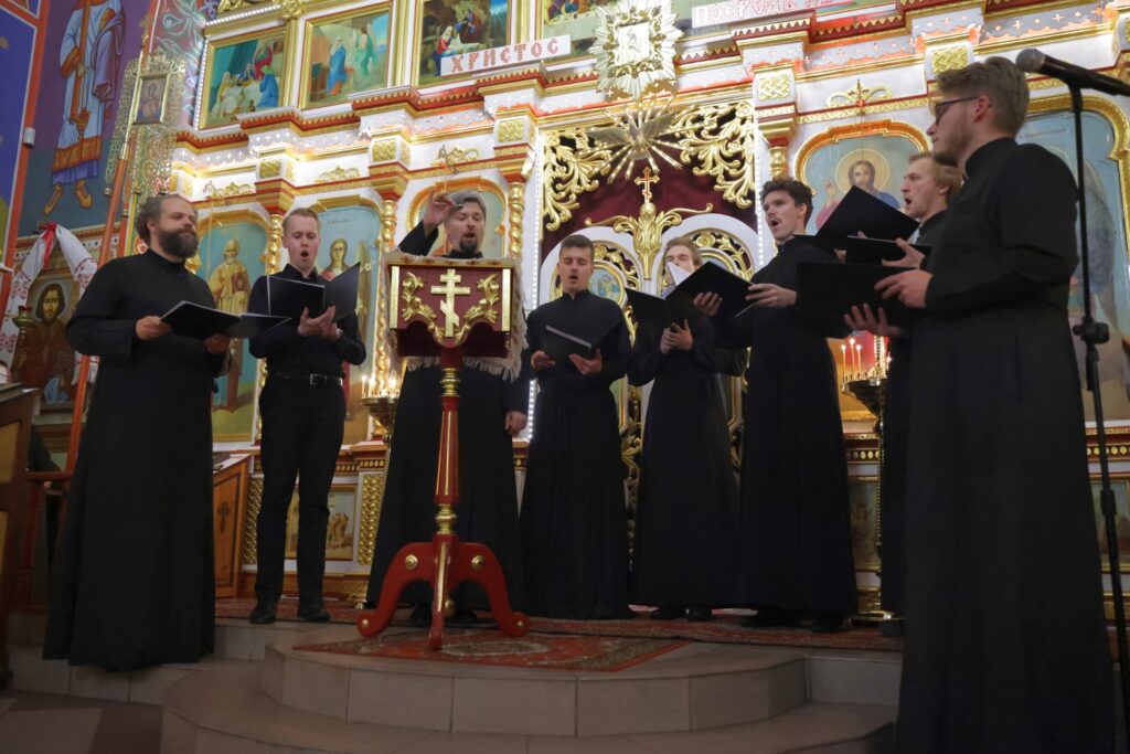 Chór męski w czerni śpiewa podczas koncertu w cerkwi.