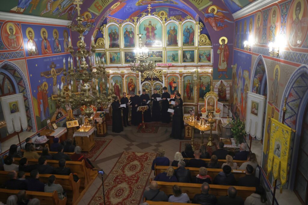 Widok z góry na cerkiew: chór śpiewa na podwyższeniu, a wierni siedzą w ławkach.