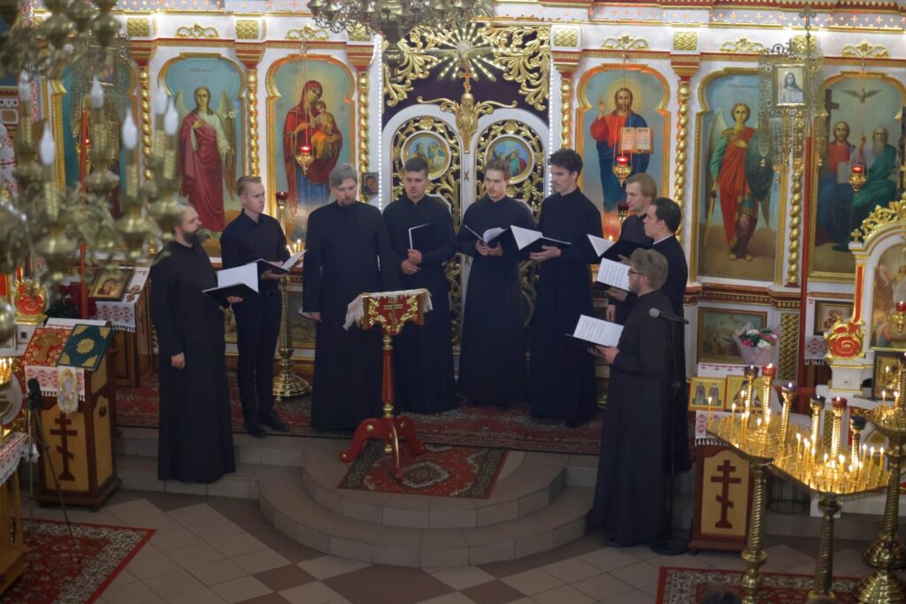 Męski chór śpiewa w cerkwi, widok z balkonu na złocony ikonostas.