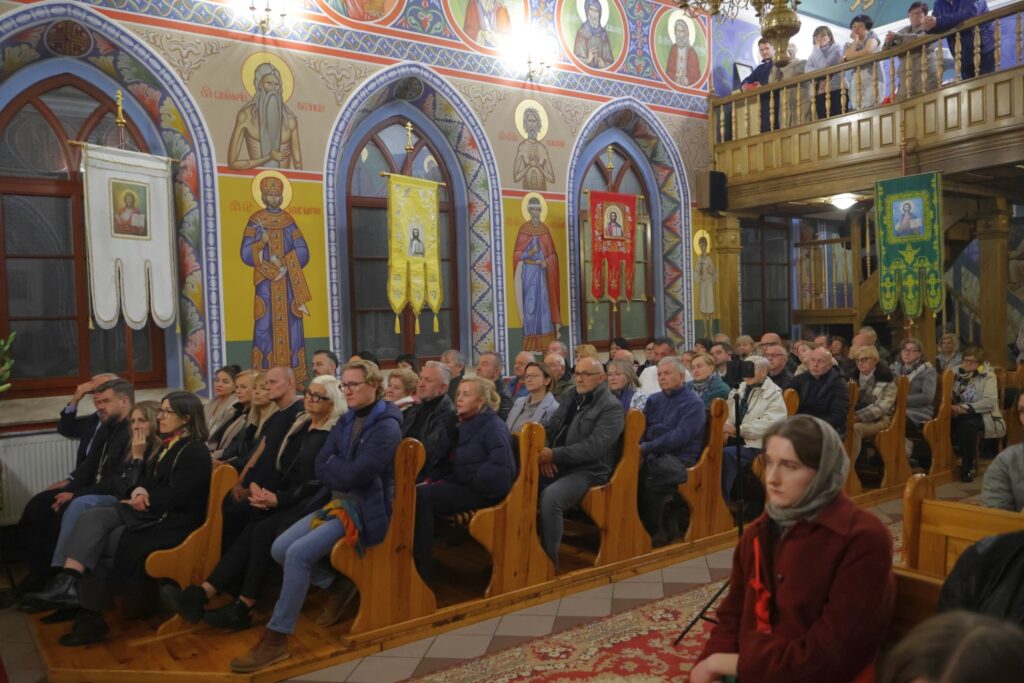 ierni słuchają koncertu, siedząc w drewnianych ławkach.