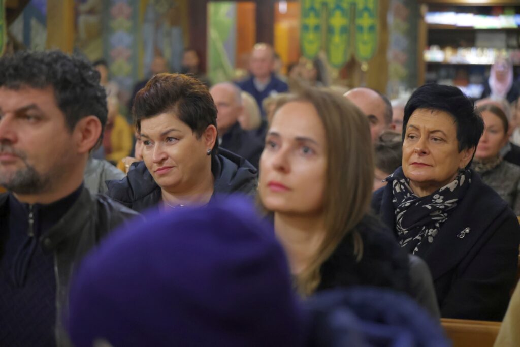 Twarze kilku słuchaczy, w tym kobiety w granatowym szaliku, podczas koncertu.