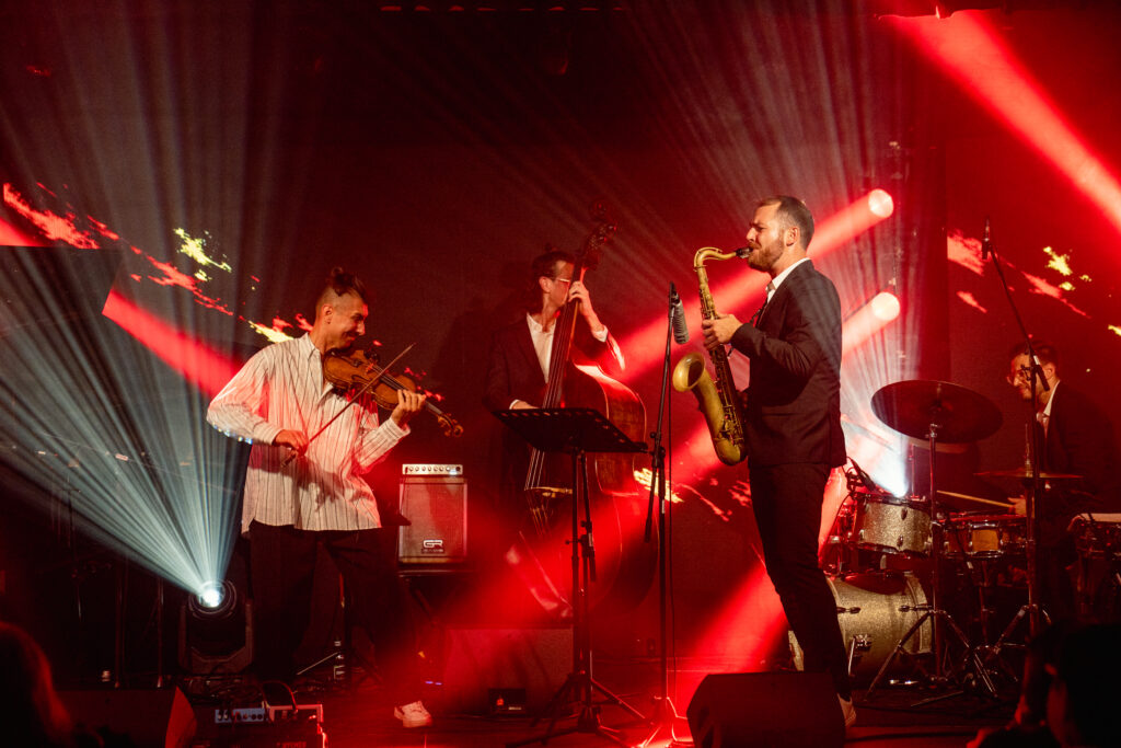 Na zdjęciu zespół jazzowy występuje na scenie, oświetlony intensywnymi czerwonymi światłami.